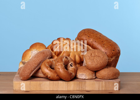 Photo of various types of bread loaves and rolls on a wooden board. Stock Photo