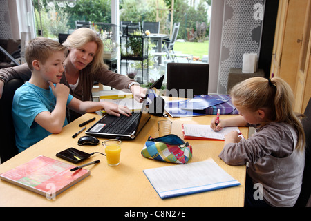 Brother and sister learning at home for school, getting assistance from their mother. Doing homework. Stock Photo