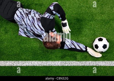 Overhead photo of a football goalkeeper diving to save the ball from crossing the goal line. Stock Photo