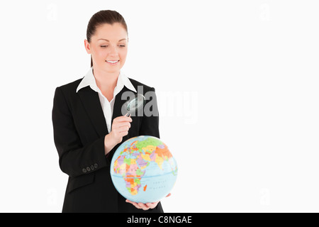 Cute female in suit holding a globe and using a magnifying glass Stock Photo