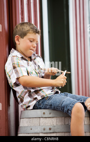 Caucasian boy sitting on barrel whittling stick Stock Photo