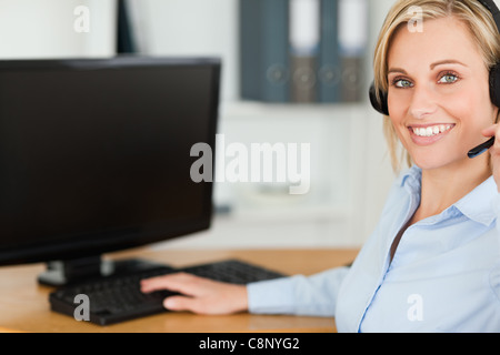Close up of a blonde businesswoman with headset working with computer looking into camera Stock Photo