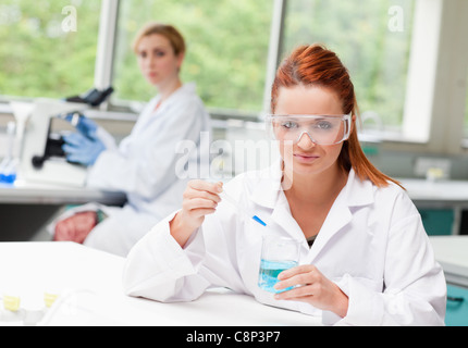 Scientist dropping liquid in a beaker while her colleague is using a microscope Stock Photo