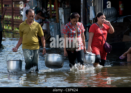 Bangkok residents carry food in metal pots, one women talks on a cel phone, through flood water from the overflowing Phra Khanong Canal,  Sukhumvit Road, soi 50, Bangkok, Thailand on October 30th, 2011. Thailand is experiencing its worst flooding in more than 50 years. credit: Kraig Lieb Stock Photo