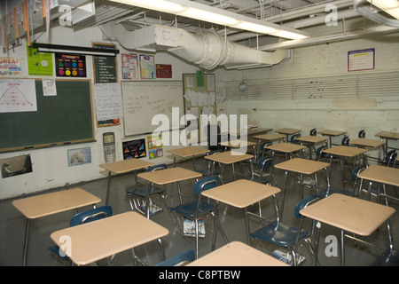 Public high school classroom overcrowded with desks, peeling paint, no windows and an exposed industrial fan for ventilation. NY Stock Photo