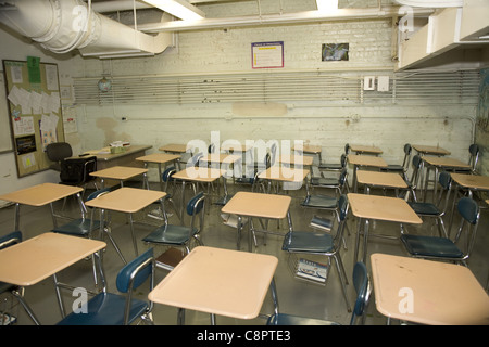 Public high school classroom overcrowded with desks, peeling paint, no windows and an exposed industrial fan for ventilation. NY Stock Photo