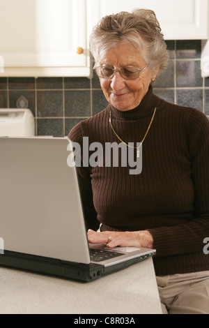 Old woman using her laptop at home. Stock Photo