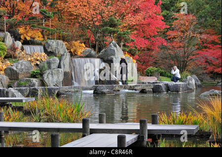 Tourists visiting Japanese garden with tree foliage in red autumn colours in the city Hasselt, Belgium