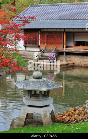 Stone lantern and pavilion / tea house in Japanese garden with tree foliage in red autumn colours in the city Hasselt, Belgium Stock Photo