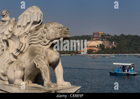 Stone lion on 17 Arch Bridge over Kunming Lake with paddle boaters at Summer Palace Beijing Peoples Republic of China Stock Photo