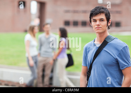 Handsome student posing while his classmates are talking Stock Photo