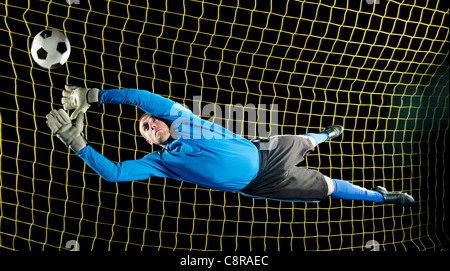 Caucasian soccer goalie jumping in mid-air catching ball at night Stock Photo