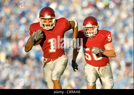 Football players running on field in game Stock Photo