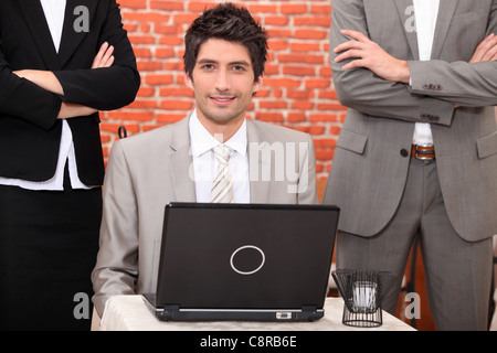 Man using a laptop flanked by people in suits Stock Photo