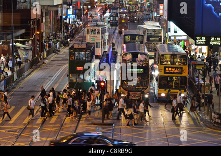 Pedestrians cross the street in front of a row of buses and trams during the busy rush hour. Stock Photo