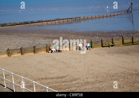 People sitting on sandy beach by wooden groynes, Hornsea, Yorkshire, England Stock Photo