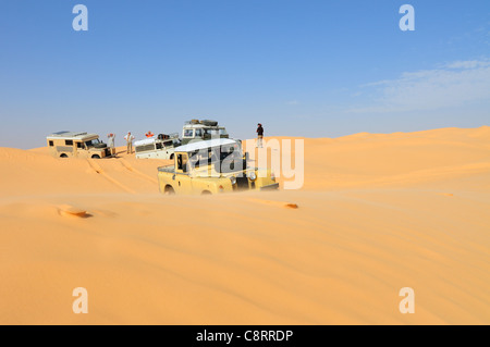 Africa, Tunisia, nr. Tembaine. Desert tourists driving historic Land Rover vehicles through a sandfield with dunes close to ... Stock Photo