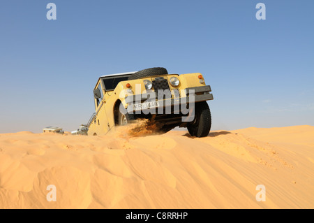 Africa, Tunisia, nr. Tembaine. Desert tourists driving historic Land Rover vehicles through a sandfield with dunes close to ... Stock Photo