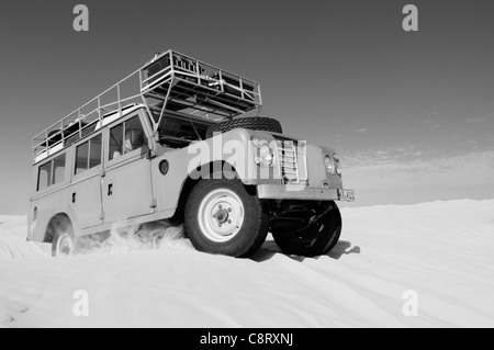 Africa, Tunisia, nr. Tembaine. Desert travellers driving their 1975 Land Rover Series 3 Station Wagon through a sandfield ... Stock Photo