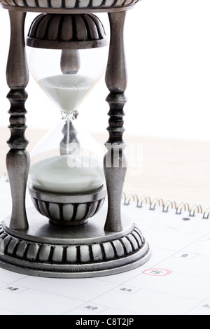 Hourglass placed on calendar against white background Stock Photo