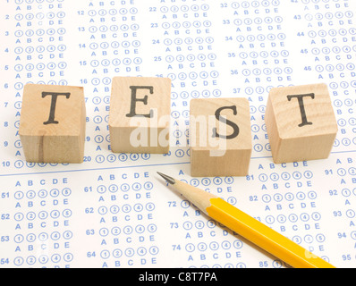 Wooden blocks spell out TEST on a blue bubble or scantron sheet with a number two yellow pencil. Stock Photo