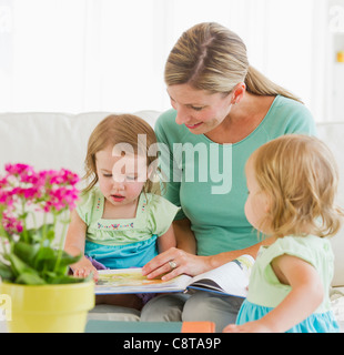 Mother with daughters reading book on sofa Stock Photo