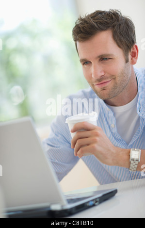 USA, New Jersey, Jersey City, Young man using laptop and drinking coffee Stock Photo