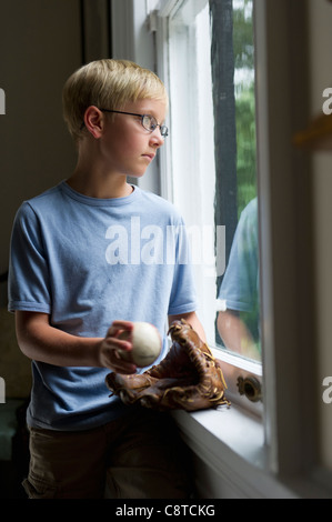 USA, New York State, Old Westbury, Boy holding baseball glove looking through window Stock Photo