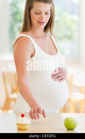 USA, New Jersey, Jersey City, Young pregnant choosing between cupcake and apple Stock Photo