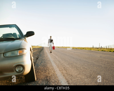 USA, Utah, Kanosh, Woman carrying canister walking along empty road, her car parked on roadside Stock Photo