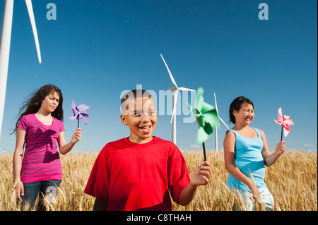 USA, Oregon, Wasco, Pre-teen girls and boy holding fans in wheat field in front of wind turbines Stock Photo