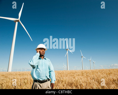USA, Oregon, Wasco, Engineer standing in wheat field in front of wind turbines, using mobile phone Stock Photo