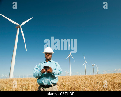 USA, Oregon, Wasco, Engineer standing in wheat field in front of wind turbines, using mobile phone Stock Photo