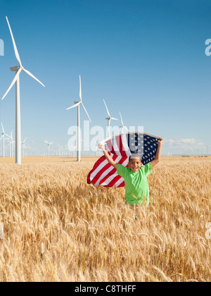 USA, Oregon, Wasco, Boy flying american flag in wheat field with wind turbines in background Stock Photo