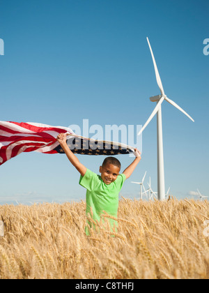 USA, Oregon, Wasco, Boy flying american flag in wheat field with wind turbines in background Stock Photo