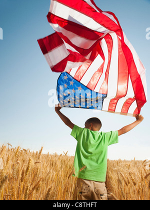 USA, Oregon, Wasco, Boy flying american flag in wheat field with wind turbines in background Stock Photo