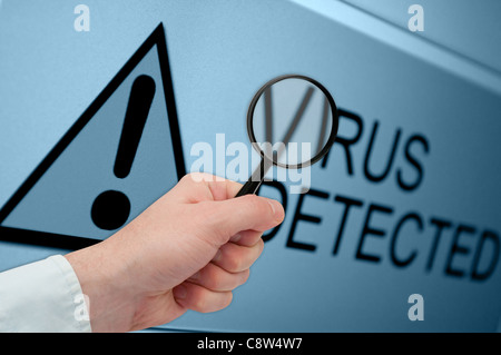 Man's Hand Holding Magnifying Glass over Virus Detected Sign on Monitor Stock Photo