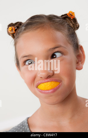 Studio portrait of girl with slice of lemon in mouth Stock Photo