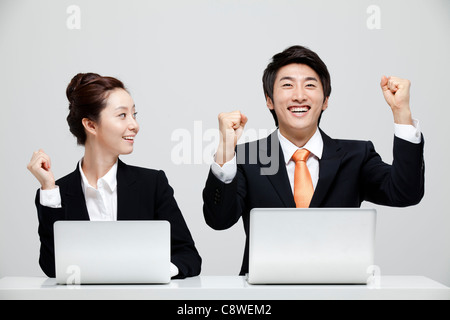 Asian Businesswoman Looking At Excited Businessman Sitting At Desk With Laptop Stock Photo