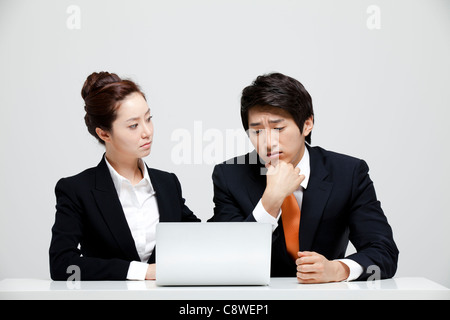 Asian Businesswoman Looking At Frustrated Businessman Sitting At Desk With  Laptop Stock Photo