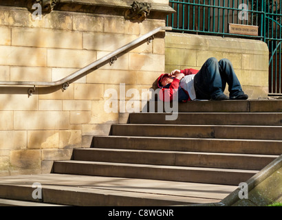 Homeless man lying on the steps of Manchester Cathedral in Manchester city centre England UK Stock Photo