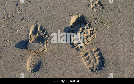 Impressions of a boot and a barefoot in the wet sand on West Wittering's beach at low tide  West Sussex, UK Stock Photo