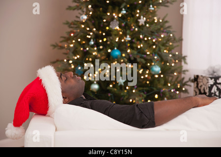 USA, Illinois, Metamora,  Man in Santa hat lying on sofa near Christmas tree Stock Photo