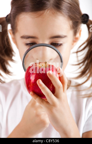 Little girl with a magnifying glass inspecting microbes on a red apple Stock Photo