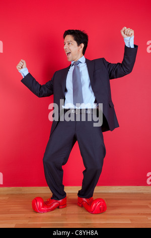 Happy businessman next to a red wall with clown shoes Stock Photo