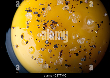 Aerial close up view of a Raw egg and egg yolk on a black reflecting surface with salt and pepper. Stock Photo