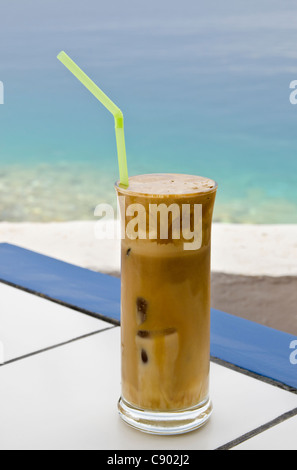 Selective focus on a Greek iced coffee, commonly known as a frappe on a table by the sea in Symi, Greece Stock Photo