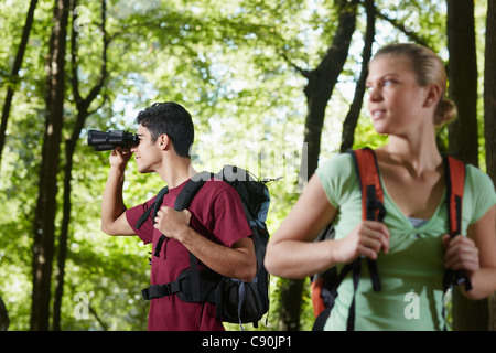 young people trekking among trees and looking at birds with binoculars. Horizontal shape, side view, waist up Stock Photo