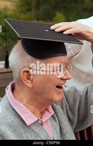 Happy Senior citizen laughing wearing a university mortarboard, also wearing glasses and hearing aid Stock Photo