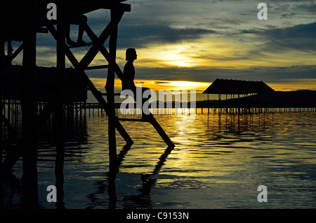 Woman silhouetted at sunset, Kri Eco Resort, Raja Ampat islands of Western Papua in the Pacific Ocean, Indonesia. Stock Photo